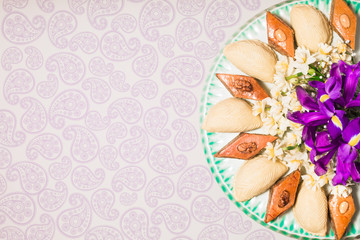 Novruz celebration plate with traditional national pastries in Azerbaijan shekerbura and pakhlava decorated with spring  flowers daffodils and purple fleur de lis silk light grey background copy space