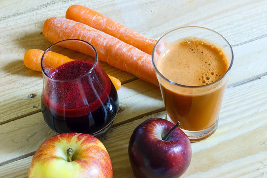 Fresh, homemade carrot and beet juice in a glass with carrots and apples on wooden background. Dieting and healthy eating concept.