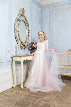 the bride in a white dress stands near a round mirror