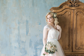 at the wardrobe stands a young bride in a white dress and holds a bouquet