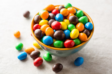 Colorful chocolate buttons in bowl on gray stone background.