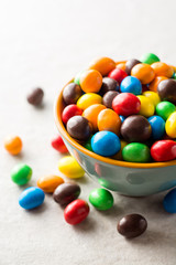 Colorful chocolate buttons in bowl on gray stone background.