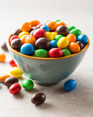 Colorful chocolate buttons in bowl on gray stone background.