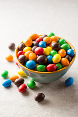 Colorful chocolate buttons in bowl on gray stone background.