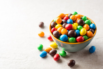 Colorful chocolate buttons in bowl on gray stone background.