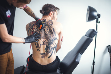 Two men in a tattoo parlor. With the help of tattoo machines, the master does a tattoo on the back...