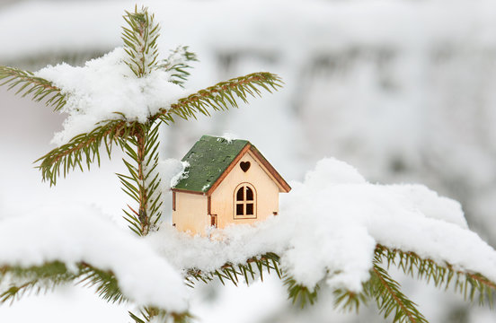 Wooden small cute toy house with green roof on сhristmas tree in snow. Cozy winter christmas or real estate concept background.