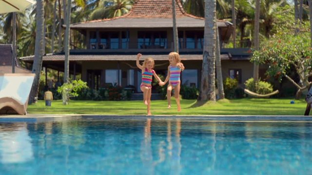 Two little cute caucasian girls jump into swimming pool at villa backyard