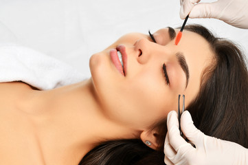 Beautician doing permanent eyebrows makeup. Closeup composition of beautiful woman face with thick...