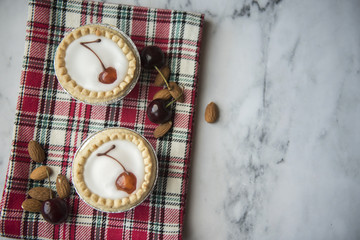 Two bakewell tarts decorated with cherries and surrounded with cherries and almonds 