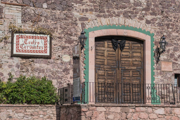 Old stone building, with the  front entrance of the Teatro Cervantes, with double wooden carved doors, a stone door frame, iron railing and theater sign, in Guanajuato, Mexico