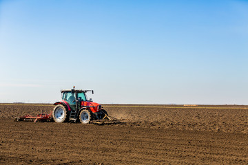 Obraz premium Farmer in tractor preparing land with seedbed cultivator as part of pre seeding activities in early spring season of agricultural works at farmlands.