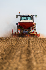 Fototapeta premium Farmer seeding, sowing crops at field. Sowing is the process of planting seeds in the ground as part of the early spring time agricultural activities.