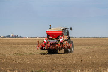 Fototapeta premium Farmer seeding, sowing crops at field. Sowing is the process of planting seeds in the ground as part of the early spring time agricultural activities.