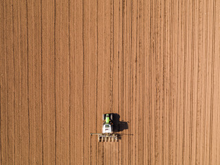 Aerial shot of a farmer seeding, sowing crops at field. Sowing is the process of planting seeds in the ground as part of the early spring time agricultural activities.