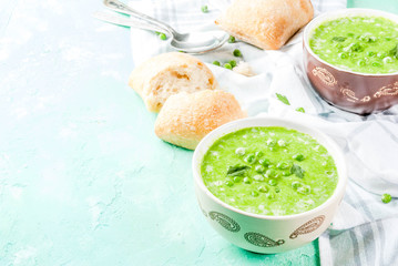 Green pea soup with fresh bread on light blue concrete table, copy space