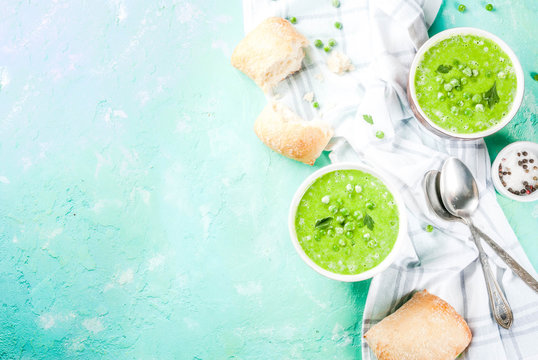 Green pea soup with fresh bread on light blue concrete table, copy space