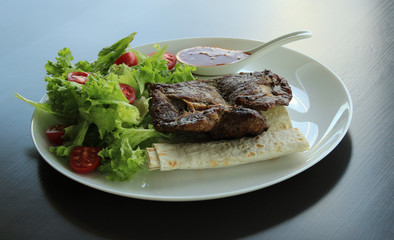 Grilled meat served with greens and pitta bread on white plate at the restaurant 