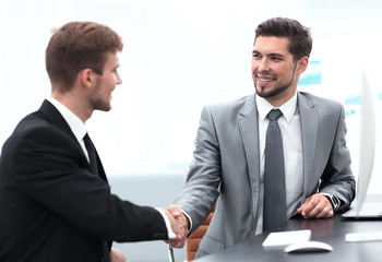 handshake of business partners sitting at a Desk.