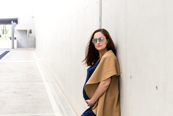 portrait of young pregnant lady with sunglasses posing near concrete wall