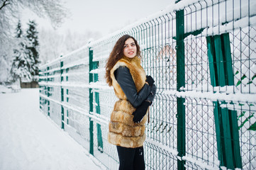 Elegance curly girl in fur coat at snowy forest park at winter.