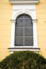 View of old stone Catholic parish building with orange brick roof, arcade window and blooming tea rose bush on a sunny summer day, Poland, Krakow