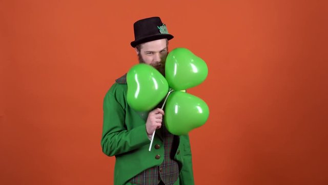 Young man leprechaun celebrating saint patrick's day isolated on orange wall with balloons