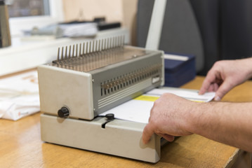 Young man using a manual paper binder to bind documents, stack of papers, together