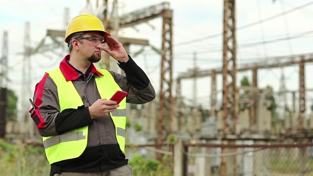 Workman at electric power plant uses smartphone. Power engineering specialist with cell phone in hand on electric power station