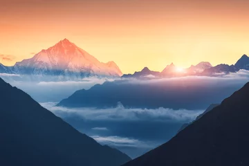Cercles muraux Himalaya Majestic scene of silhouettes of mountains and low clouds at colorful sunrise in Nepal. Landscape with snowy peaks of mountains, beautiful sky and yellow sunlight. Rocks and sun rays.Nature background