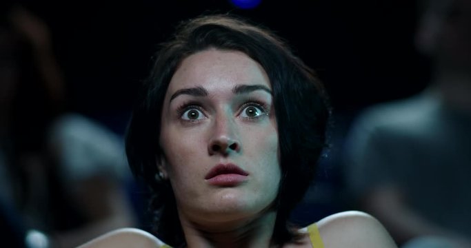 Frightened woman in a cinema watching a horror film. Jumps at a scary moment