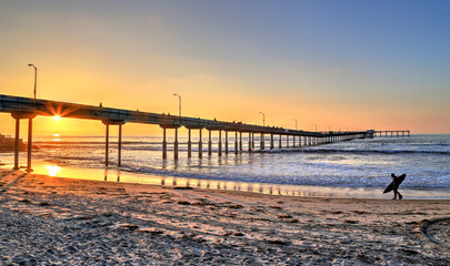 A surfer walks on Ocean Beach near the pier in San Diego, California. - obrazy, fototapety, plakaty