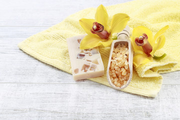 Scoop of sea salt, bar of handmade soap and two yellow orchid flowers.