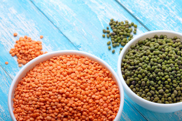 Fototapeta premium Red lentils and green bean or mung bean in bowl on a blue wooden table.Copy space.Top view