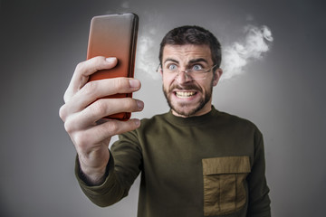 Young man angry with his cell phone, yelling at it, letting off steam and burning his phone with rage - obrazy, fototapety, plakaty