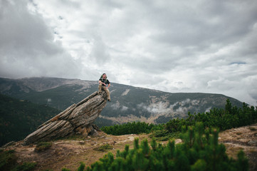 male tourist sits on a high rock above the coniferous green fore