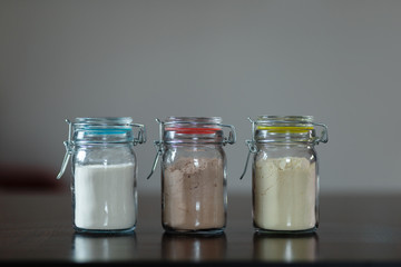 Three glass jars with protein powder, strawberries, banana and chocolate for dilution with milk or water. Sports and dietary nutrition for athletes and weight loss or muscle gain bodybuilders.