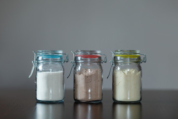 Three glass jars with protein powder, strawberries, banana and chocolate for dilution with milk or water. Sports and dietary nutrition for athletes and weight loss or muscle gain bodybuilders.