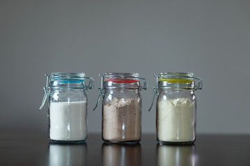 Three glass jars with protein powder, strawberries, banana and chocolate for dilution with milk or water. Sports and dietary nutrition for athletes and weight loss or muscle gain bodybuilders.