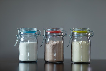 Three glass jars with protein powder, strawberries, banana and chocolate for making milk shakes. Sports and dietary nutrition for athletes and weight loss or muscle mass bodybuilders.