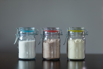 Three glass jars with protein powder, strawberries, banana and chocolate for dilution with milk or water. Sports and dietary nutrition for athletes and weight loss or muscle gain bodybuilders.