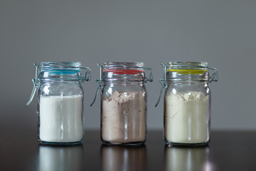Three glass jars with protein powder, strawberries, banana and chocolate for making milk shakes. Sports and dietary nutrition for athletes and weight loss or muscle mass bodybuilders.