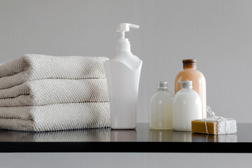 Obraz na płótnie Canvas Stack of towels with shampoo, conditioner, shower milk and handmade soap. Neutral background.
