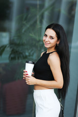 Young beautiful business woman drinks coffee near beside office building