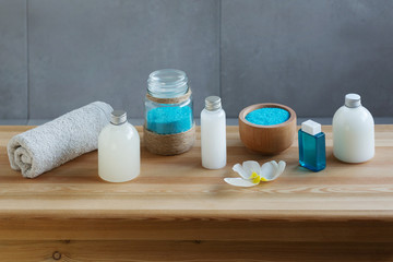 Towel, small bottles of milk for shower, shampoo, conditioner and a wooden bowl of sea salt scrub. Spa concept.