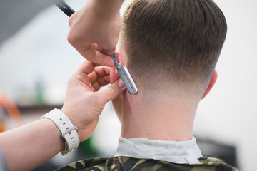 The hairdresser makes a stylish men's hairstyle with a dangerous razor. Barber shaves a man's shawl...