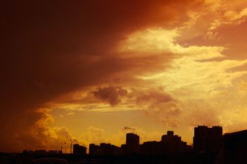 Beautiful colorful dramatic sunset sky with stormy clouds over silhouette of the city.