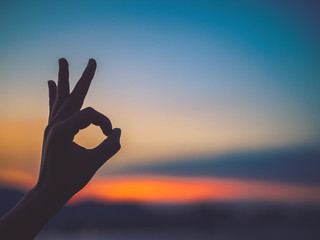 Closeup and silhouette of woman hands make Ok hand sign during  sunset background. Hope concept.