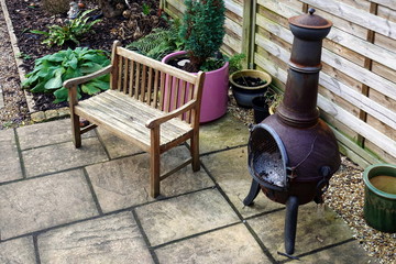 Wooden bench, chiminea and various plants, some in pots, in a small domestic courtyard garden in winter
