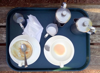 A tray with finished tea and coffee cups, and stainless steel jugs, outside on a wooden table